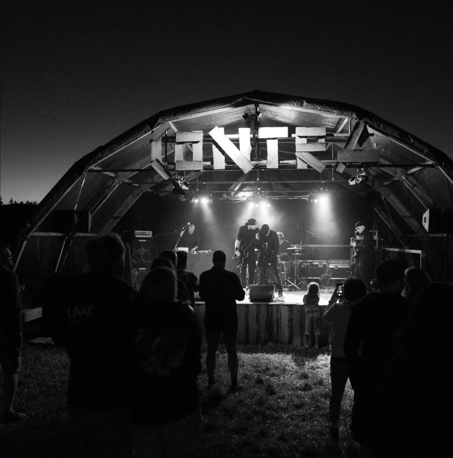BROOK performing live outdoors at night under a wooden festival stage roof